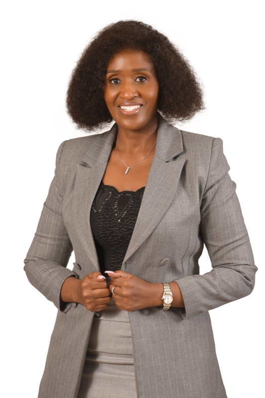 Anne Musau, arms crossed and confident, in a grey check blazer